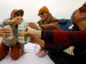 3 people with jackets and hats/beanies "cheers" their beers from Cape May Brewing Co.