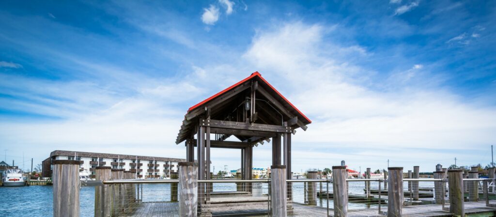 Panoramic shot of the wooden pier and covered gazebo at a Cape May-Lewes Ferry terminal, highlighting the scenic Delaware Bay view under a bright blue sky.